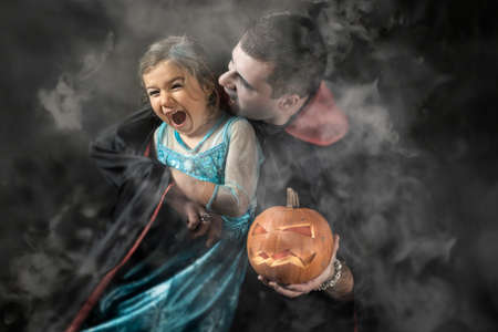 Halloween portrait vampire attacking young princess father and daughter play adult Caucasian white man holding orange pumpkin smoke or fog backgroundの写真素材
