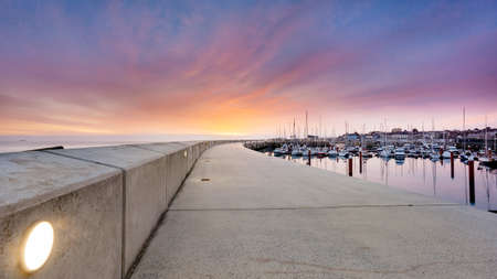 Amazing sky on sunrise at Greystones yacht marina or harbour with anchored boats and long illuminated pier. County Wicklow, Irelandの写真素材