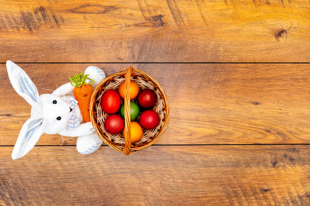 Seven colourful Easter eggs in pastel colours in the basket and Easter bunny holding carrot on...