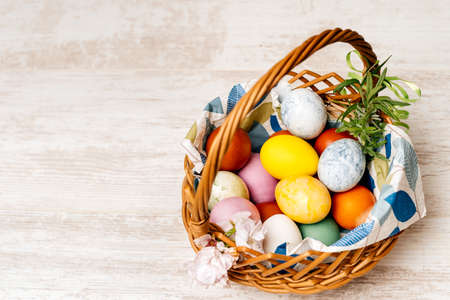 Polish traditional wicker basket full of multi coloured and mottled Easter eggs. Basket decorated with flowers on vintage oak table or background.の写真素材