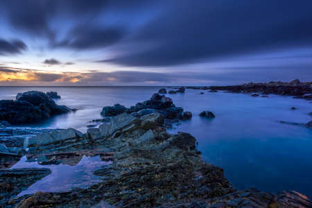 Twilight begins yielding to daylight at rocky coastline with blurred water and sky, long exposure photography. Northern Irelandの写真素材