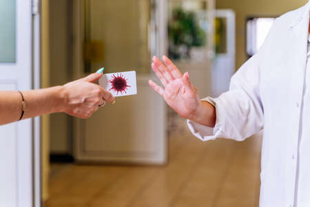 Middle age, female doctor in hospital corridor, showing stop with hand or palm to coronavirus or covid 19 spread of contagious diseaseの写真素材