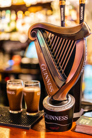 Dublin, Ireland, August 2018 Selective focus on Guinness tap with blurred pints of foamy beer and wall of bottles. Guinness is iconic Irish beerのeditorial素材