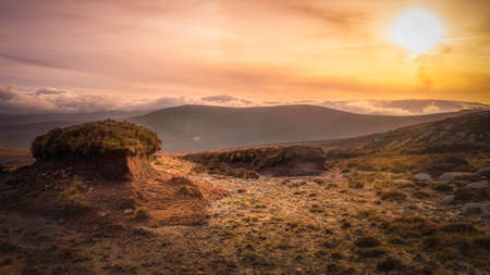 Island of old cut turf or peat, highlighted by setting sun in beautiful scenery of Wicklow mountains. Dramatic sunset and cloudscape at golden hourの写真素材