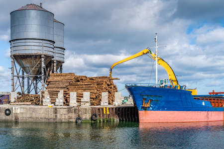 Crane with wood logs gripple loading timber on cargo ship for export in Wicklow commercial port. Transport industry in Irelandの写真素材