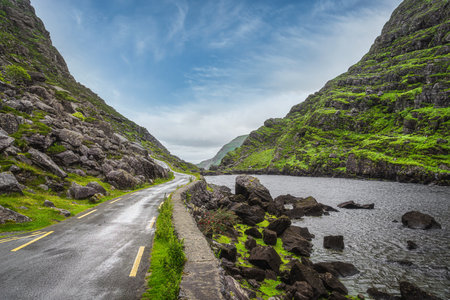 Narrow winding road running alongside lake and stream in green valley, Gap of Dunloe in Black Valley, Ring of Kerry, County Kerry, Irelandの素材 [FY310161983870]