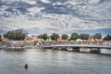 Zadar, Croatia, July 2019 Pedestrians crossing bridge, Gradski most, with walled old town in background and marina with moored motorboats in a bayのeditorial素材