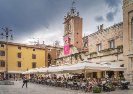 Zadar, Croatia, July 2019 Tourists relaxing in outdoor restaurant and beer garden in the square of old town with St. Lawrence Church in backgroundのeditorial素材