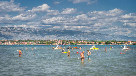 Nin, Croatia, July 2019 People relaxing and having fun in water of Adriatic Sea, Zdrijac beach with mountain range of Dinaric Alps in the backgroundのeditorial素材