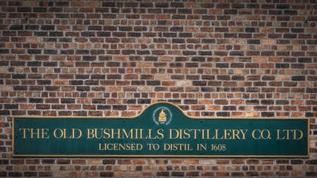 Bushmills, Northern Ireland, Aug 2019 The Old Bushmills Distillery Co. Ltd Licensed to distil in 1608 sign on rustic brick wallのeditorial素材