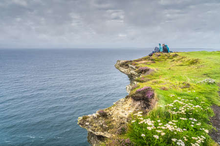 Group of young people sitting on the edge of cliff on iconic Cliffs of Moher, popular tourist attraction, Wild Atlantic Way, County Clare, Irelandの写真素材