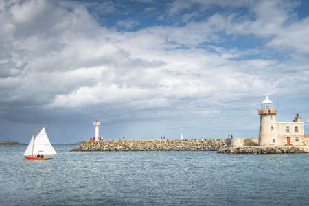 People on a small sailboat exiting Howth marina, passing Howth Lighthouse and per, Dublin, Irelandの写真素材