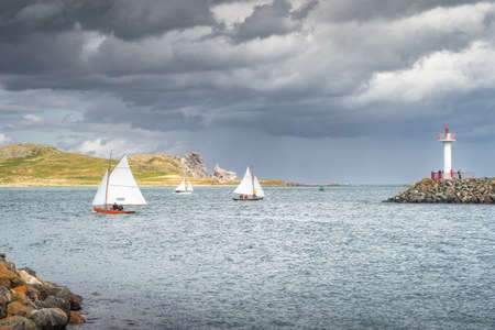 People on a small sailboats exiting Howth marina, passing Howth Lighthouse and per with Irelands Eye island in the background, Dublin, Irelandの写真素材