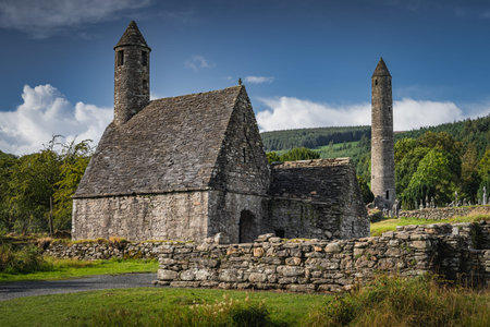 Medieval church, ancient graves, Celtic crosses in Glendalough Cemetery with forest and mountains in...