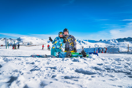 Couple, skier and snowboarder sitting on the snow and looking at camera, Pyrenees Mountains. Winter ski holidays in El Tarter, Grandvalira Andorraの写真素材
