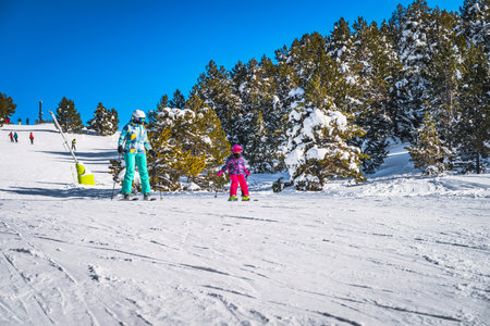 Mother and daughter skiing down a slope on a winter ski holidays in Andorra, El Tarter Snowy forest in Pyrenees Mountainsの写真素材