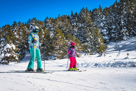 Closeup of mother and daughter skiing down a slope on a winter ski holidays in Andorra, El Tarter. Snowy forest in Pyrenees Mountainsの写真素材