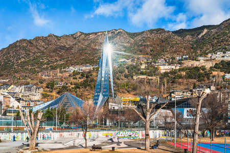 Andorra la Vella, Andorra, Jan 2020 People having fun on skatepark, aquapark with glass tower reflecting sun and Pyrenees Mountains in backgroundのeditorial素材