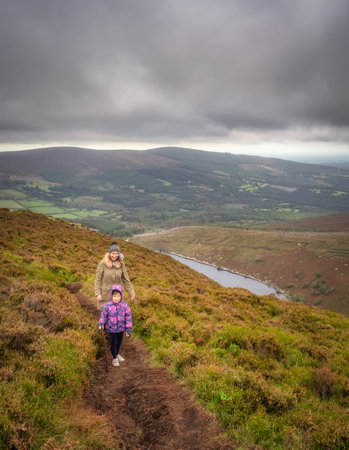 Mother and daughter hiking on a hilltop around the lake, Lough Bray, surrounded by dramatic storm clouds. Family hiking in Wicklow Mountains, Irelandの写真素材