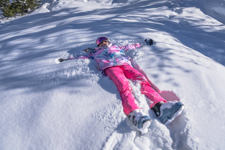 Young girl in ski equipment, smiling and making snow angel in deep snow in the mountains, Montgenevre ski village, France, Alpsの写真素材