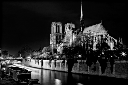 Black and white photograph of Notre Dame Cathedral at night from the rear with a boat and a barge on the river Seine in Paris, France.の写真素材