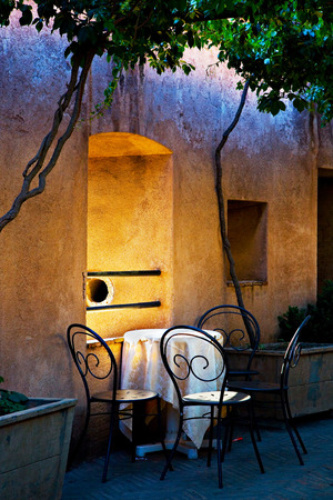 Four chairs and a table in a romantic setting under small trees, next to a window in a yellow and purple wall の写真素材