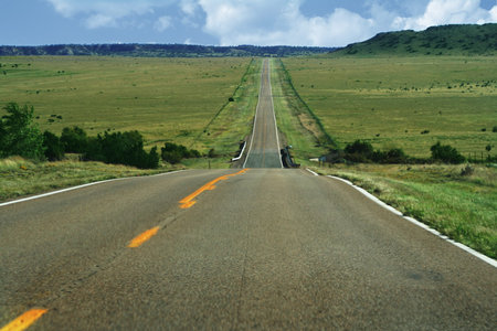 a long, open road disappearing in the distance into some low hills.  Green pastures and a blue...