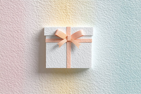 Clean white gift box with delicate peach ribbon and bow on a textured watercolor paper background.の素材