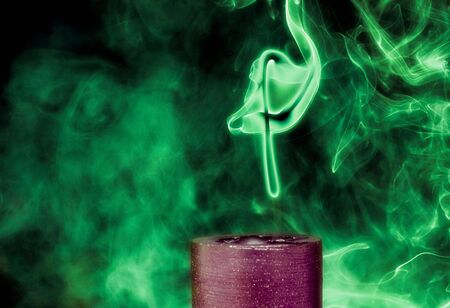 Recently extinguished, a single candle billows forth a swarm of smoke that shapes itself into a cryptic symbol.の写真素材