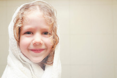 Little curly girl in towel in bathroom after shower, close up.