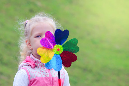 Little curly blonde girl holding multicolored pinwheel in her hands.