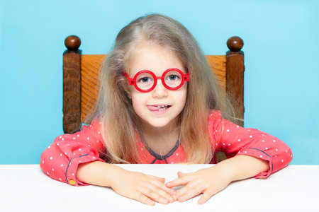 Funny little blonde girl with glasses looking at the camera stuck out her tongue.の写真素材