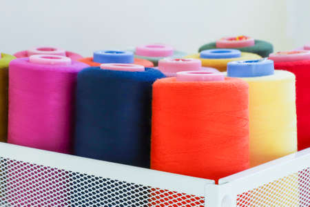 Sewing threads on spool in the white metal grid box, multicolored background, closeup.の写真素材