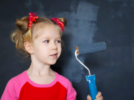 Little funny smiling girl paint the wall with magnetic paint.