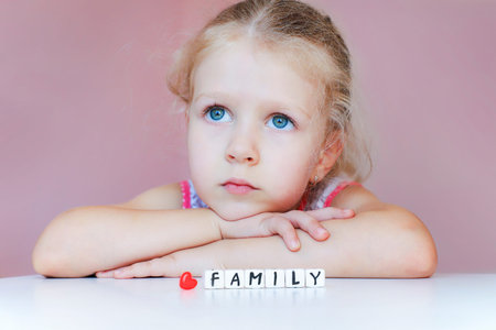 Little sad girl dream about family. Protect your family concept. With hands on chin looking up. Word...