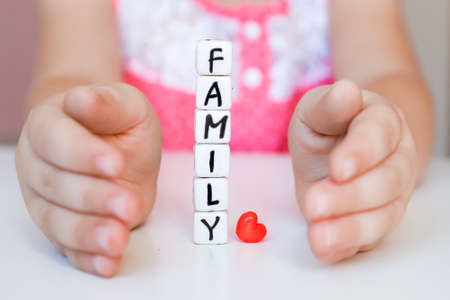 Little girl hold toy blocks with word Family. Protect your family concept. Word Family made of plastic blocks.の写真素材