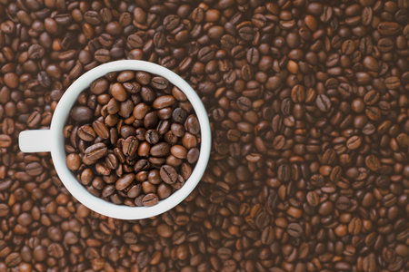 White cup with coffee beans on the coffee beans background.