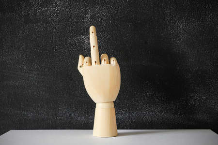 Wooden hand showing a middle finger standing on the white table on the black chalkboard background.の写真素材