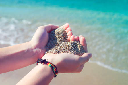 The girl at the sea holds sand in her hands in the shape of a heart.の写真素材