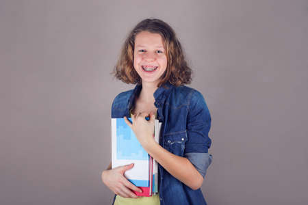 Young smiling curly hair girl with braces on teeth holds books in her hands.の写真素材