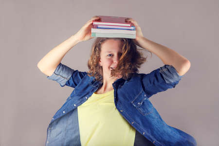 Young spinning smiling curly hair girl with braces on teeth holds books on her head.の写真素材
