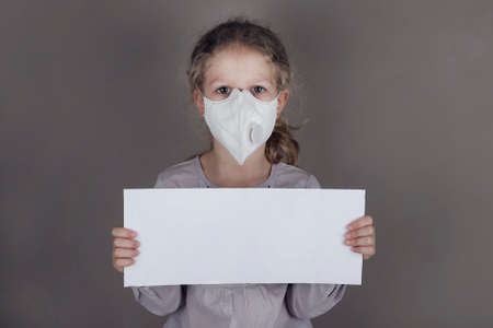 Little girl in medical mask is holding blank white poster on a gray background.の写真素材