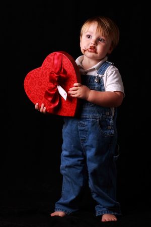 toddler holding a box of chocolates with chocolate all over his faceの写真素材