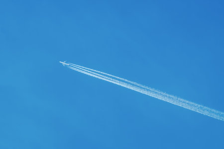 Jet airliner flying high in the sky, leaving contrails in the clear blue skyの写真素材