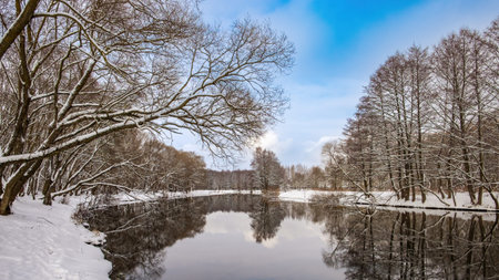 Winter landscape. The river surface of the water, blue sky, snow on the banks, reflections of trees...