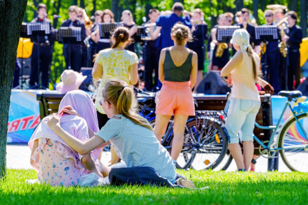Minsk, Belarus - May 09, 2018: Girls on the lawn listening to a brass band in the park. Minsk...