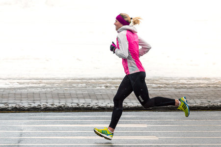 Minsk, Belarus - March 08, 2018: A female athlete running in winter outside in cold snowy weather....
