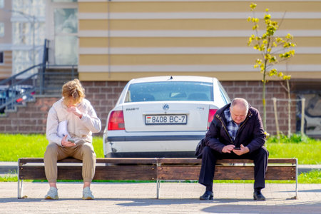 Minsk, Belarus - May 18, 2022: People and mobile phones. A young man and an elderly man at a public transport stop look at the screens of their mobile phones.のeditorial素材