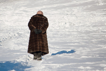 Very old woman walks alone on a path in the snow