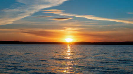 Idyllic sunset on the water. Sailboat on the background of the setting sun. Warm colorsの写真素材